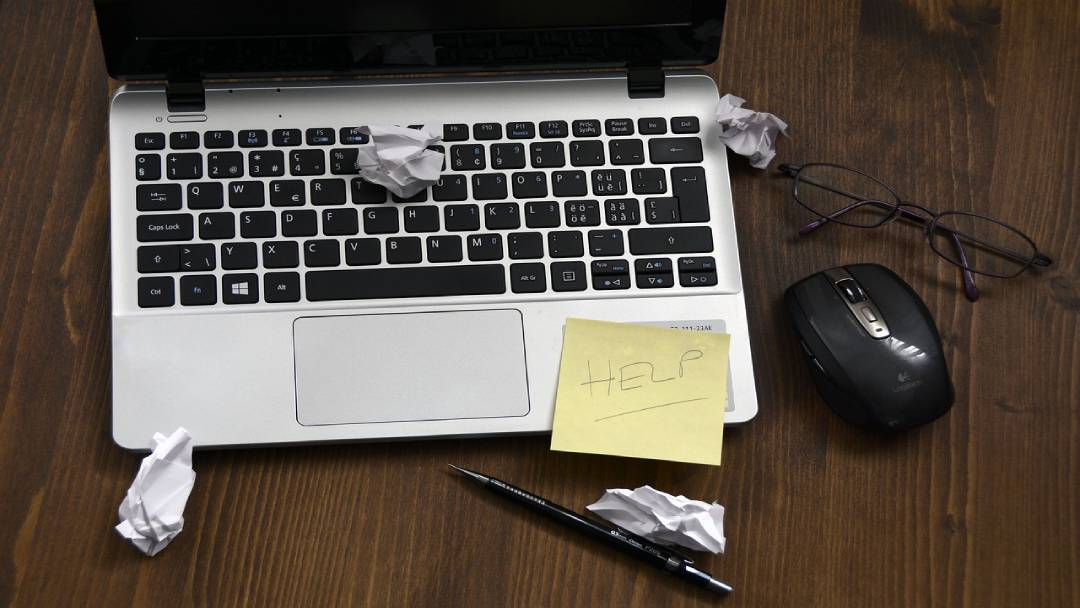 Laptop with crumbled papers and help note