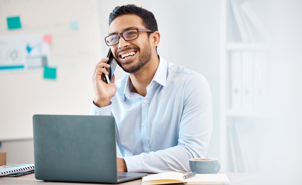 Confident employee using a laptop and mobile phone — illustrating the rise of modern VoIP and Zoom Phone alternatives for Canadian businesses.