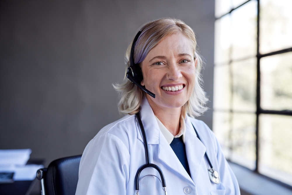 Healthcare professional using SE Telecom cloud phone systems for healthcare smiling in clinical office environment with headset