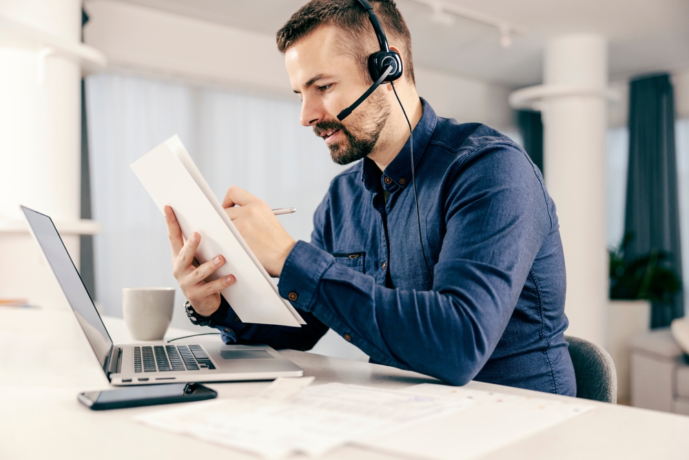 Canadian IT manager reviewing his VoIP telephone migration plan with SE Telecom on headset and laptop in a modern office