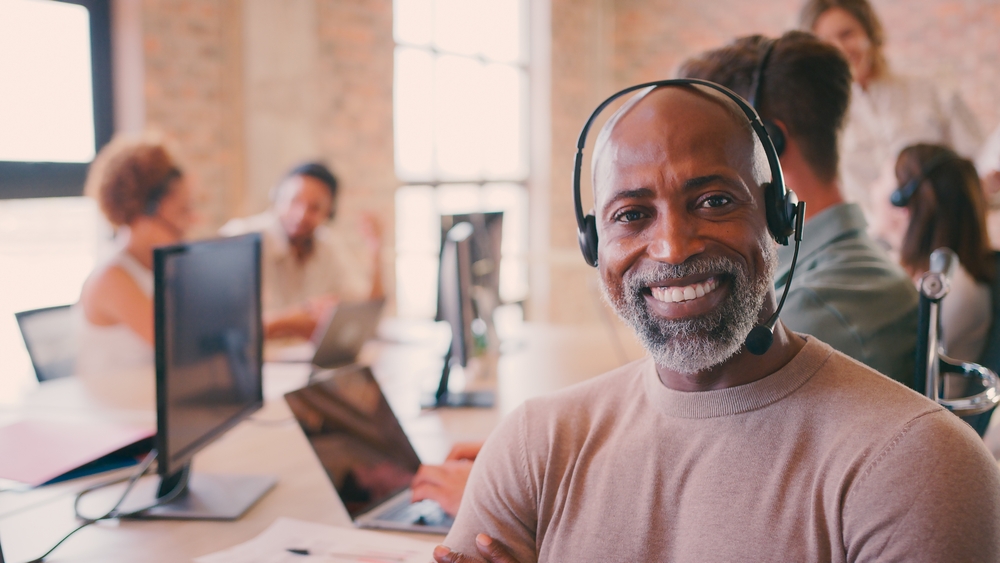 Winnipeg business leader smiling on headset during SE Telecom VoIP Winnipeg deployment in a modern collaborative office environment