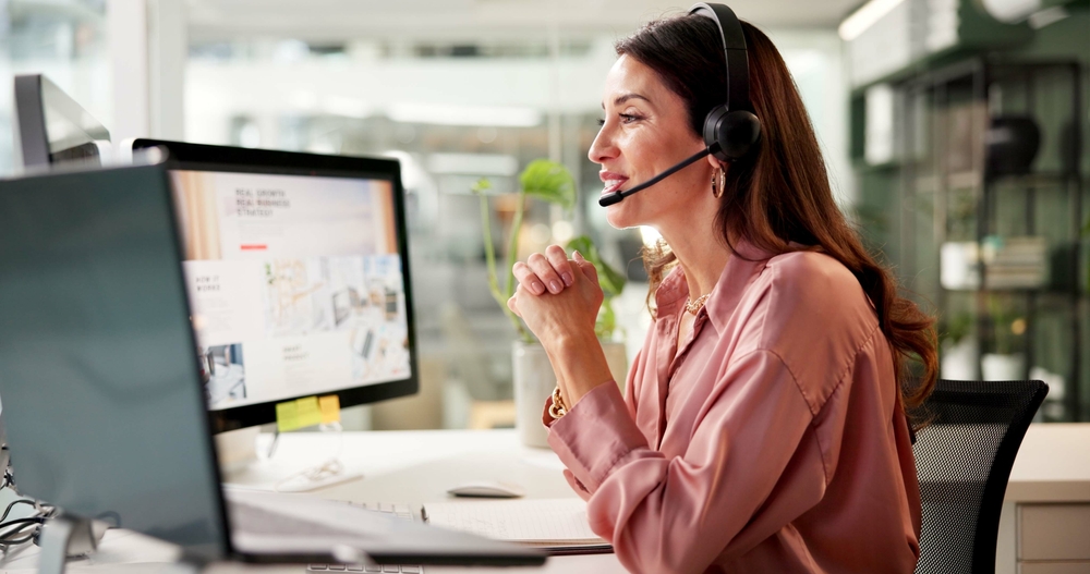 Woman,,Mic,And,Computer,Screen,At,Call,Center,In,Office Support agent smiling while wearing a headset and working within a cloud based contact center dashboard